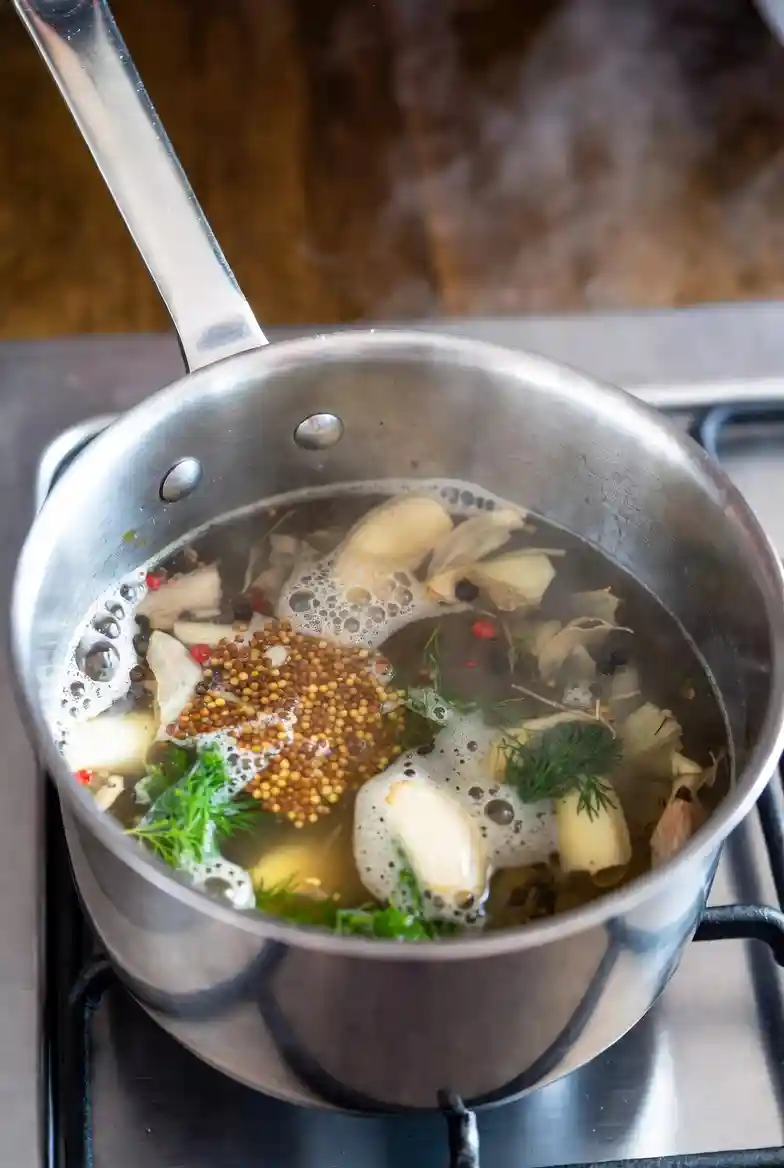 A saucepan on a stove with vinegar, water, sugar, and spices gently simmering, creating a flavorful homemade pickling brine for preserving eggs or vegetables.