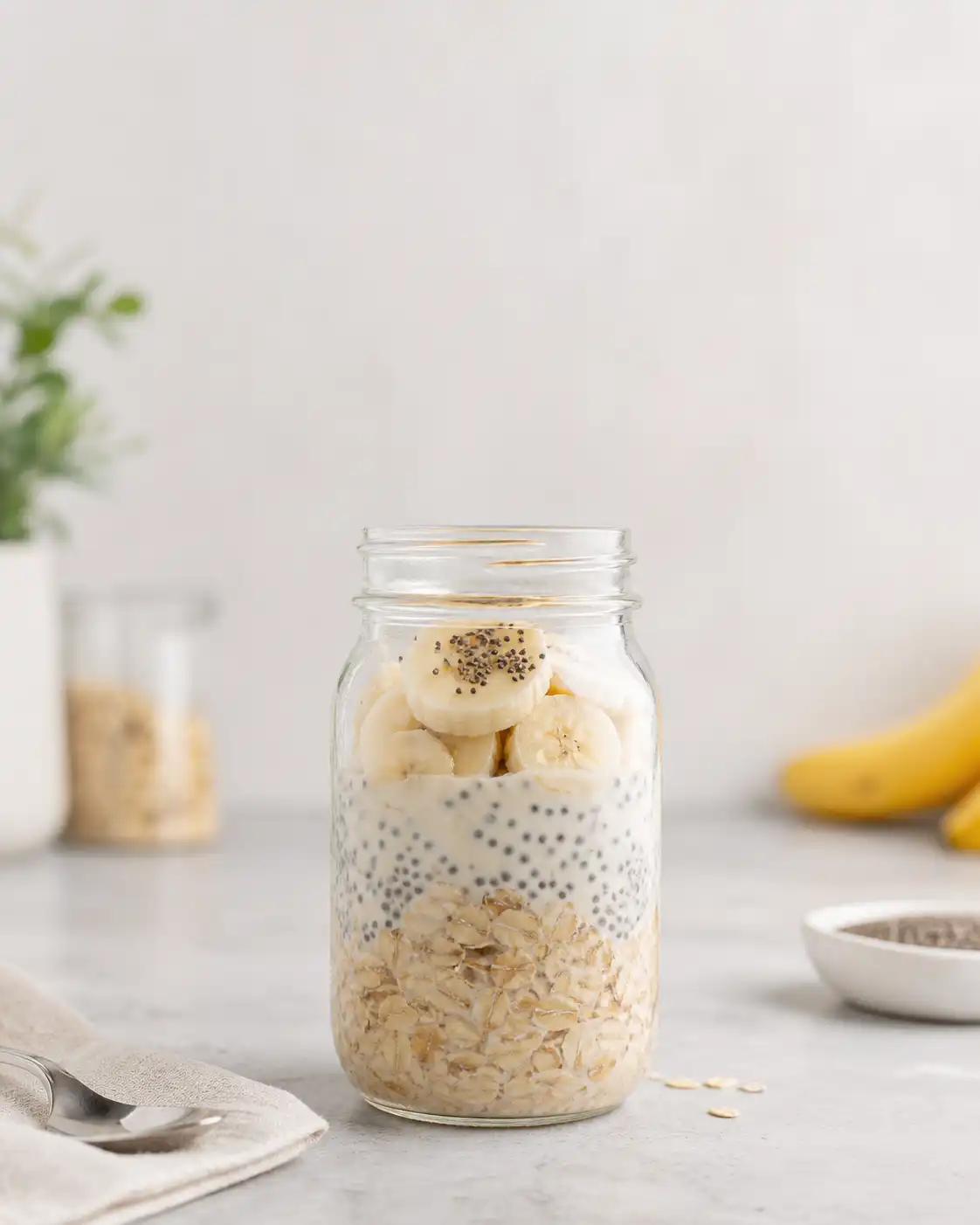 Glass mason jar filled with layers of overnight oats, chia seeds, and sliced bananas.