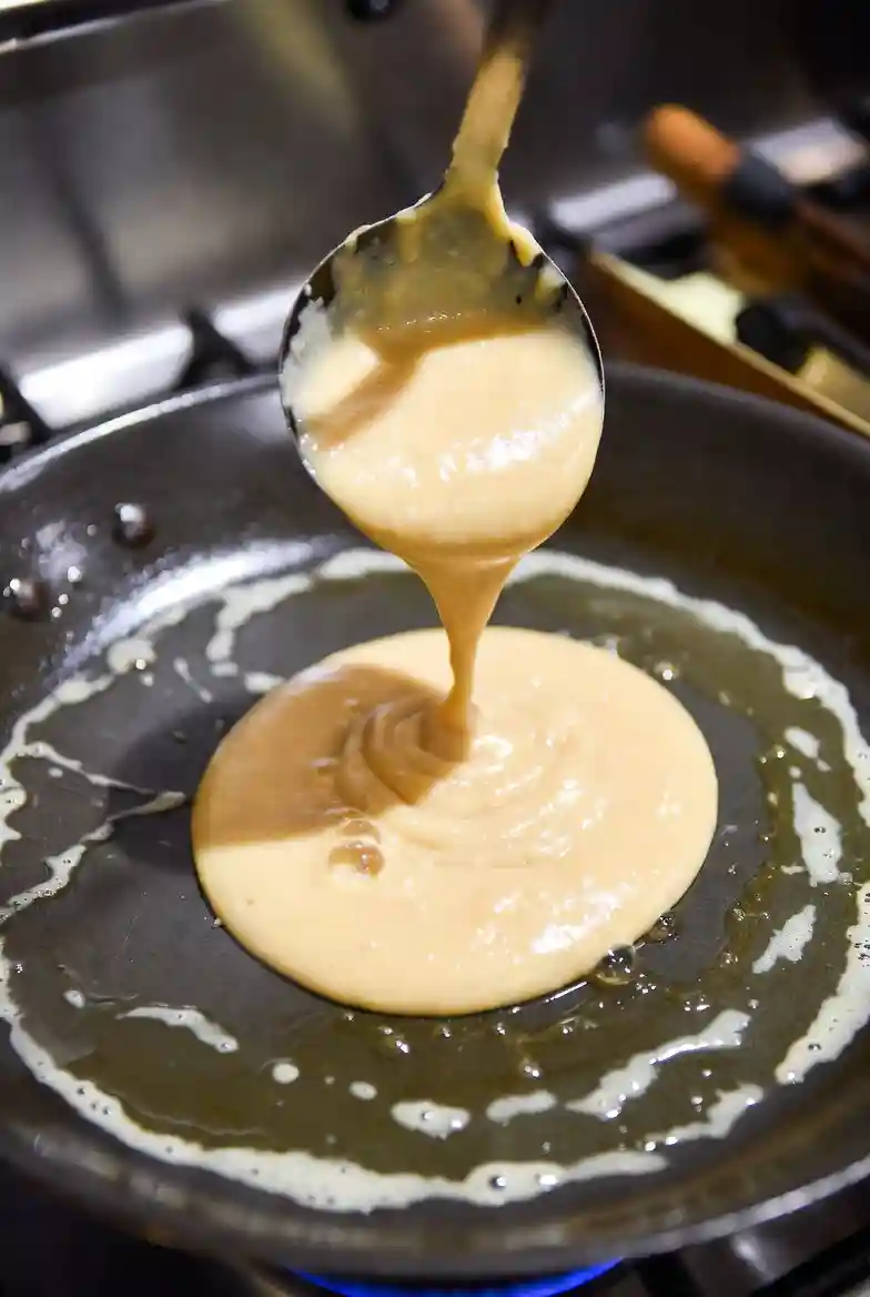 A ladle pouring thick pancake batter onto a hot buttered griddle, forming a round shape as small bubbles begin to appear on the surface while cooking starts.Select 73 more words to run Humanizer.