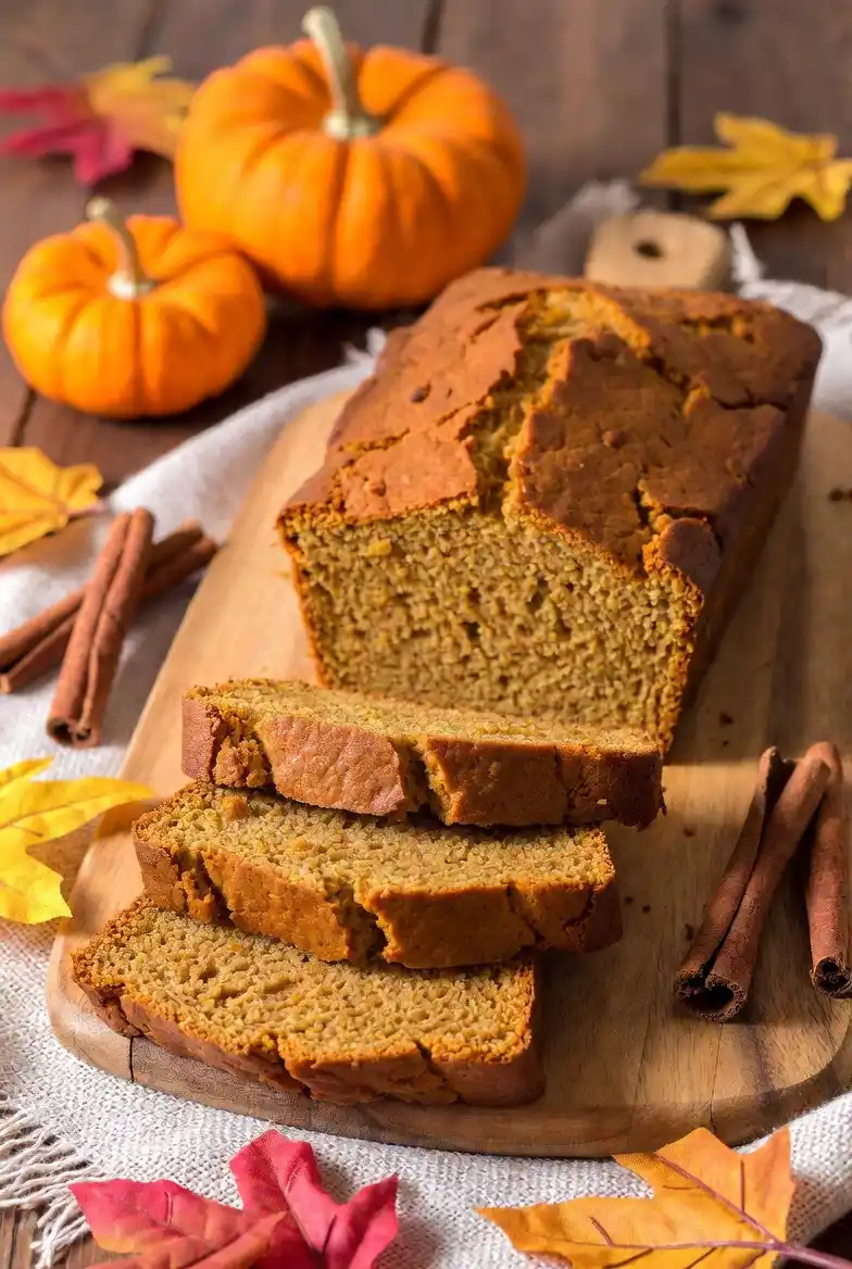 A styled arrangement featuring pumpkin bread surrounded by small pumpkins, cinnamon sticks, and autumn leaves, creating a warm and cozy fall-themed baking display.
